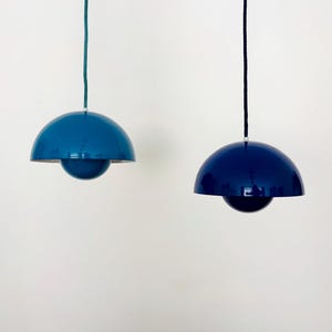 May include: Two pendant lights with a modern design. One is a medium blue, the other is a deep navy blue. Each has a rounded, dome-shaped shade and a spherical bottom. The lights hang from a cord.