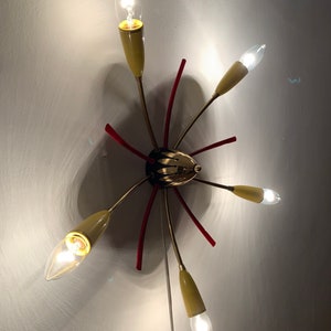 May include: A gold and red ceiling light fixture with six light bulbs. The light fixture has a starburst design with red accents.