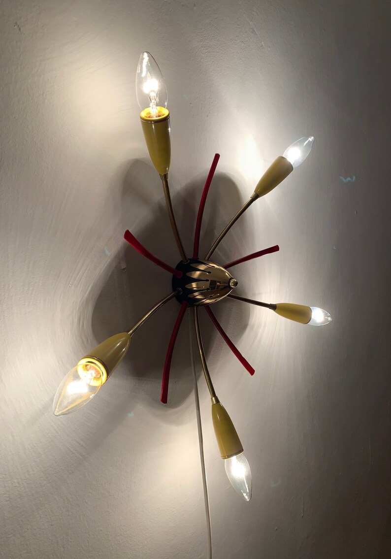 May include: A gold and red ceiling light fixture with six light bulbs. The light fixture has a starburst design with red accents.