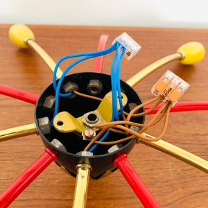 May include: Close-up of the wiring and connectors for a multi-arm ceiling light fixture. The fixture has six arms, each with a red and gold finish. The wiring is connected to a black electrical box with multiple screws.