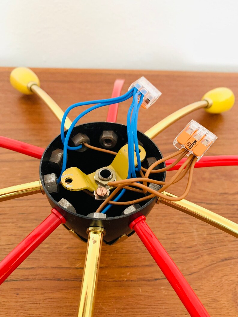 May include: Close-up of the wiring and connectors for a multi-arm ceiling light fixture. The fixture has six arms, each with a red and gold finish. The wiring is connected to a black electrical box with multiple screws.