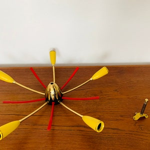 May include: A gold-toned, six-armed chandelier with yellow glass shades and red accents. The chandelier is disassembled and laid out on a wooden surface.