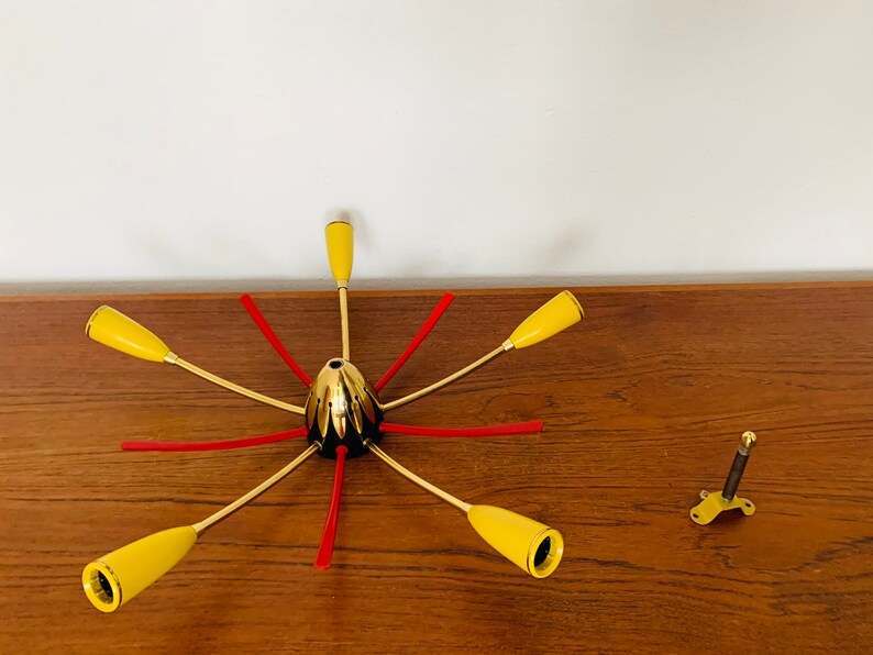 May include: A gold-toned, six-armed chandelier with yellow glass shades and red accents. The chandelier is disassembled and laid out on a wooden surface.