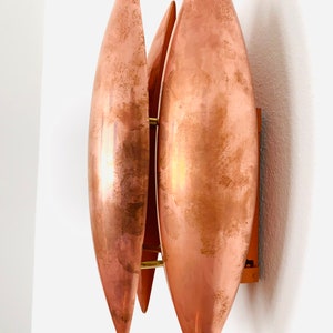 May include: A copper wall sconce with three overlapping, teardrop-shaped shades. The shades are a warm copper color and have a slightly textured surface.
