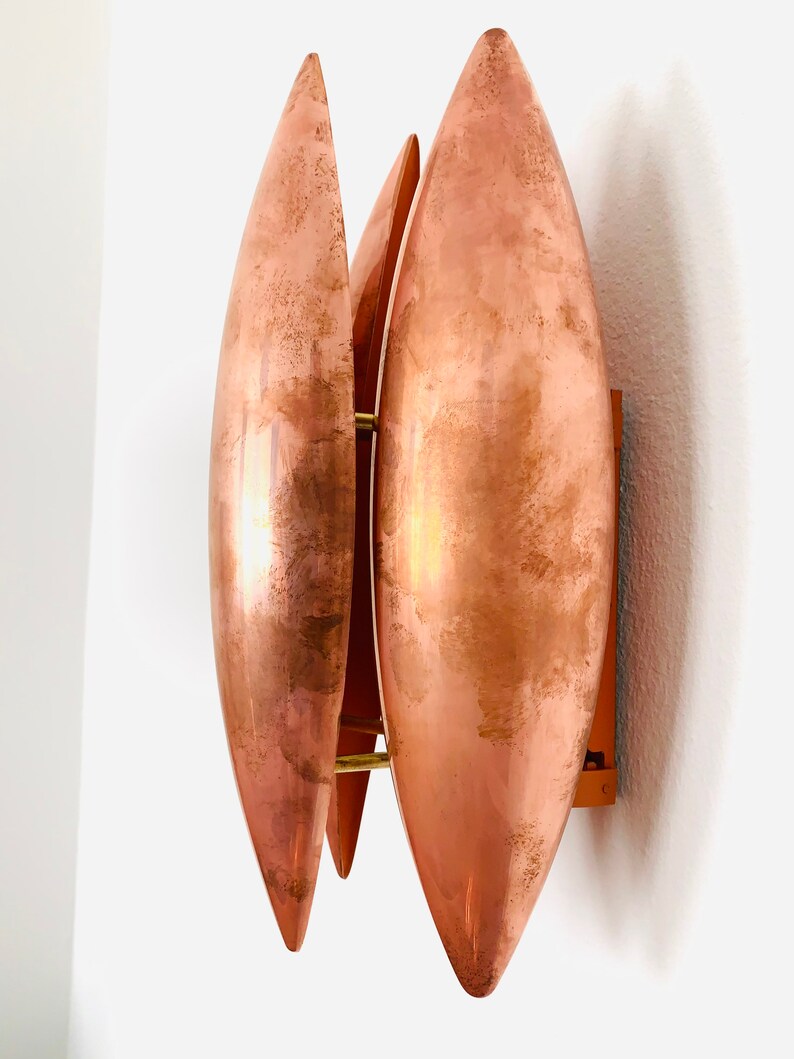 May include: A copper wall sconce with three overlapping, teardrop-shaped shades. The shades are a warm copper color and have a slightly textured surface.