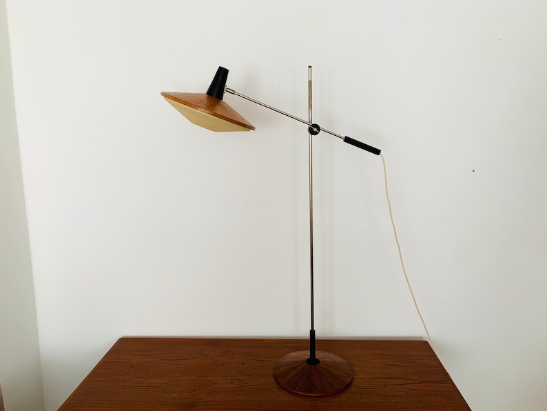 Puede incluir: Una l&aacute;mpara de pie moderna de mediados de siglo con una pantalla de madera y metal. La l&aacute;mpara tiene una base de metal plateado y un brazo negro.