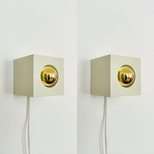 May include: Two white square wall sconces with gold spherical light fixtures. The sconces have a simple, modern design.