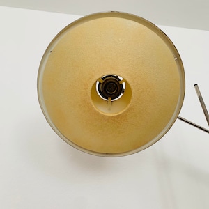 Puede incluir: Una pantalla de l&aacute;mpara redonda de color blanco y amarillo con un marco de metal. La pantalla es redonda y tiene una peque&ntilde;a abertura en el centro.
