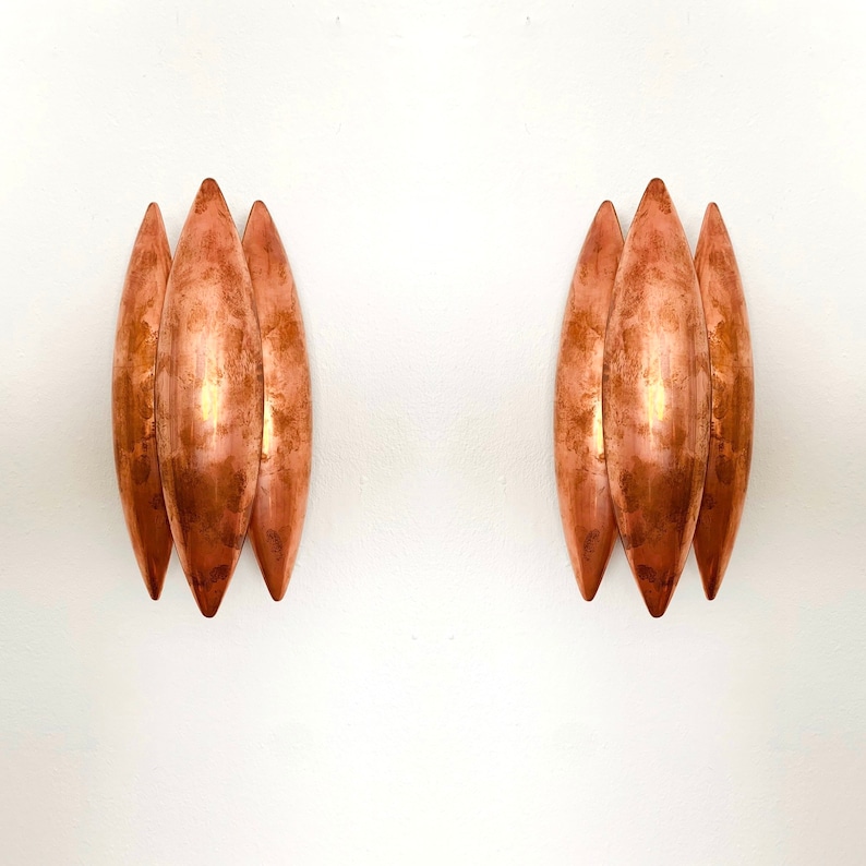 May include: Two sets of copper wall sconces, each with three overlapping, teardrop-shaped shades.