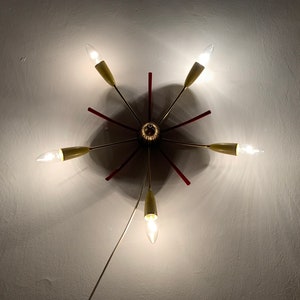 May include: A gold and red ceiling light fixture with six light bulbs. The light fixture has a starburst design with red accents.