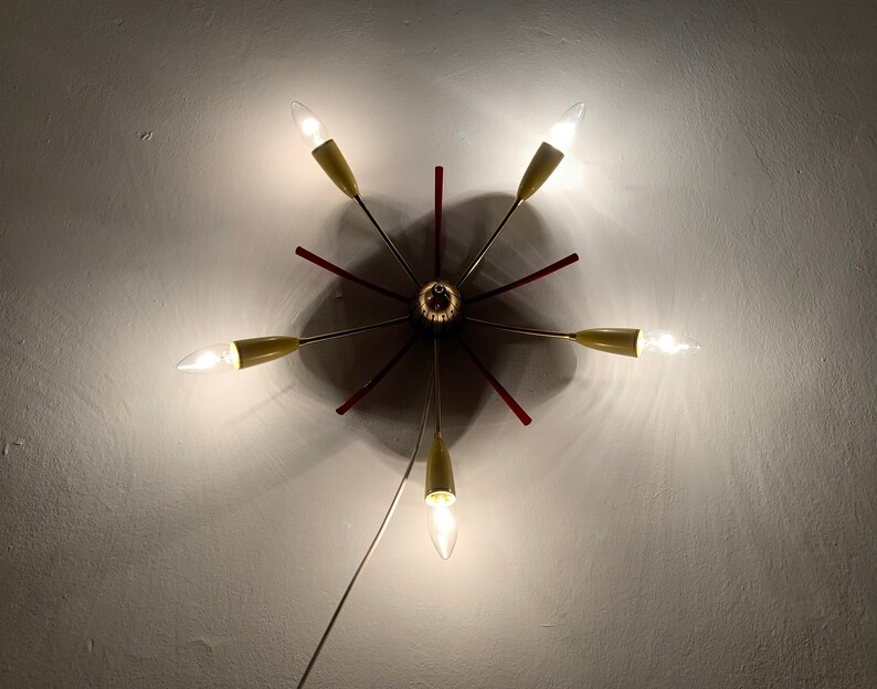 May include: A gold and red ceiling light fixture with six light bulbs. The light fixture has a starburst design with red accents.