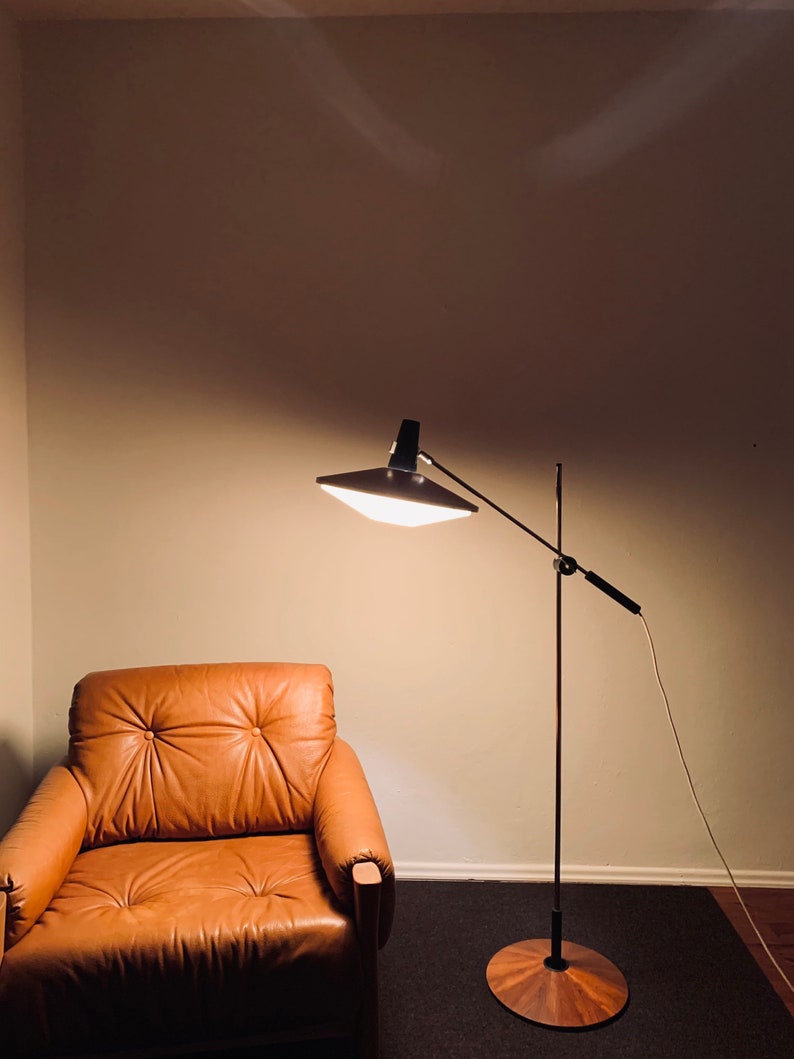 Puede incluir: Un sill&oacute;n de cuero marr&oacute;n se encuentra frente a una l&aacute;mpara de pie negra con una pantalla blanca y una base de madera. La l&aacute;mpara est&aacute; encendida y proyecta luz sobre el sill&oacute;n.