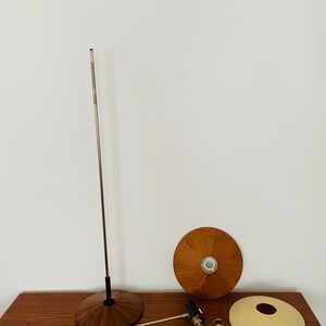 Puede incluir: Una l&aacute;mpara moderna de mediados de siglo desmontada con una base y una pantalla de madera. La l&aacute;mpara tiene un poste de metal plateado y un cable negro.