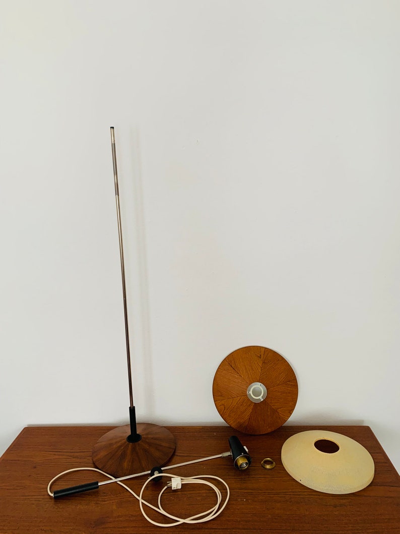 Puede incluir: Una l&aacute;mpara moderna de mediados de siglo desmontada con una base y una pantalla de madera. La l&aacute;mpara tiene un poste de metal plateado y un cable negro.