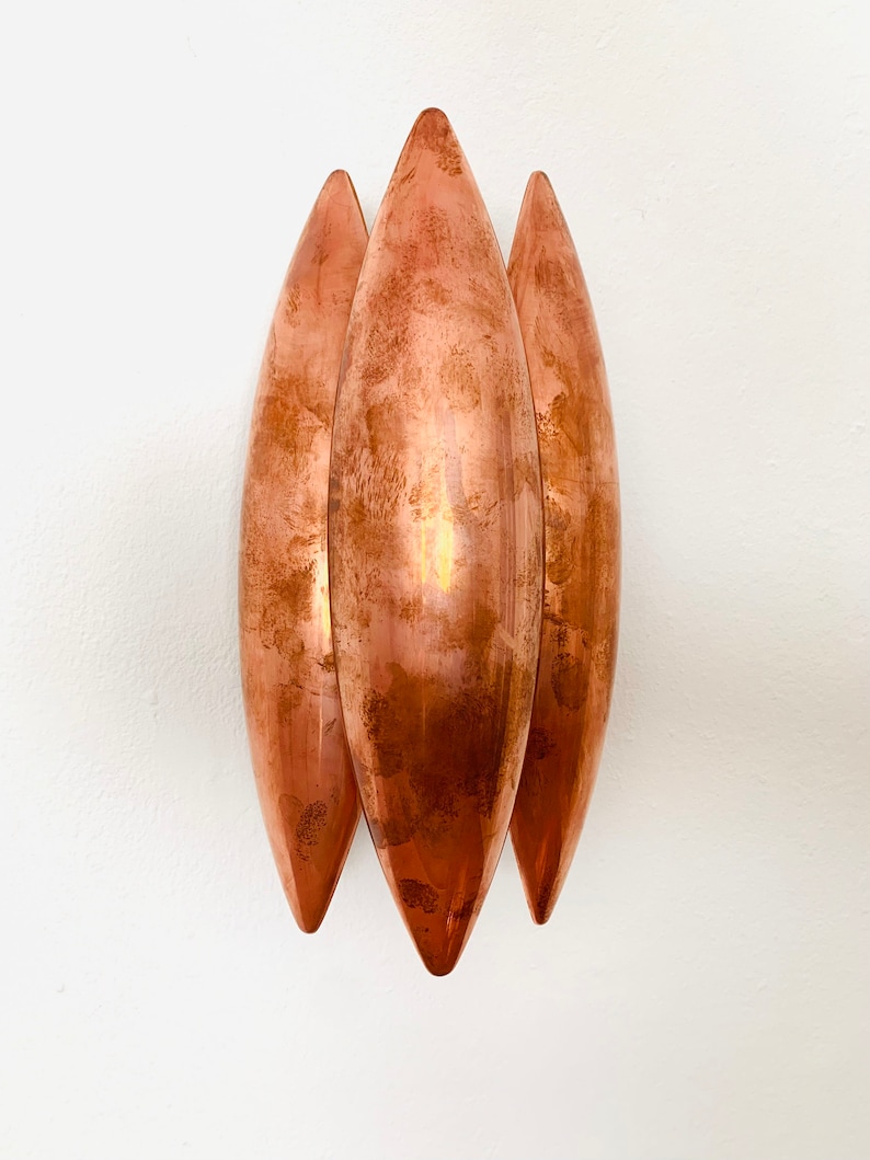 May include: Three copper wall sconces in the shape of elongated teardrops, mounted on a white wall.
