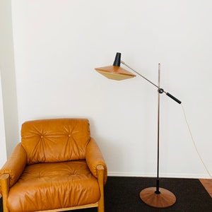 Puede incluir: Un sill&oacute;n de cuero marr&oacute;n con marco de madera se encuentra sobre una alfombra marr&oacute;n oscuro. Una l&aacute;mpara de pie con base de madera y una pantalla marr&oacute;n y negra se encuentra en el fondo.