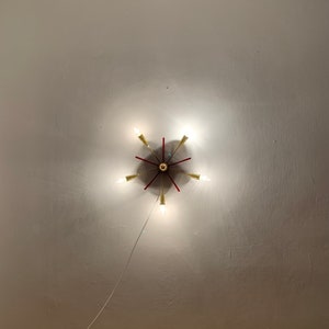 May include: A gold and red ceiling light fixture with six light bulbs. The light fixture is mounted on a white ceiling.