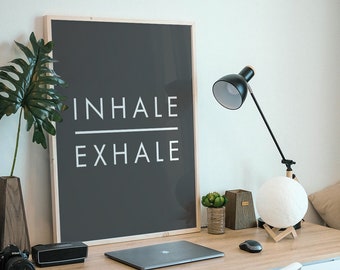 Könnte beinhalten: Ein gerahmtes Schwarzweiß-Poster mit den Worten "INHALE EXHALE" auf grauem Hintergrund. Das Poster hängt an einer weißen Wand über einem Holztisch mit einem Laptop, einer Lampe und einer Topfpflanze.