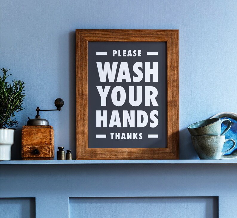 Puede incluir: Un letrero enmarcado con el texto "PLEASE WASH YOUR HANDS THANKS" en blanco sobre un fondo gris oscuro. Un molinillo de caf&eacute; de madera, pesas peque&ntilde;as y dos tazas verde azulado est&aacute;n en una estanter&iacute;a azul.