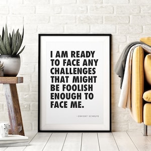May include: Black and white framed print with a quote from the TV show "The Office" by Dwight Schrute. The quote reads: "I am ready to face any challenges that might be foolish enough to face me."