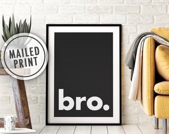 Puede incluir: Impresión artística enmarcada en negro con la palabra "bro." en blanco sobre un fondo negro. La impresión se muestra sobre un suelo de madera blanco, con una pared de ladrillo blanco al fondo. Una pegatina "MAILED PRINT" es visible.