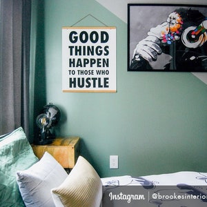 May include: A motivational wall art print with the text "GOOD THINGS HAPPEN TO THOSE WHO HUSTLE" in black on a white background. The print is hanging on a green wall. A framed black and white monkey art print is also visible.