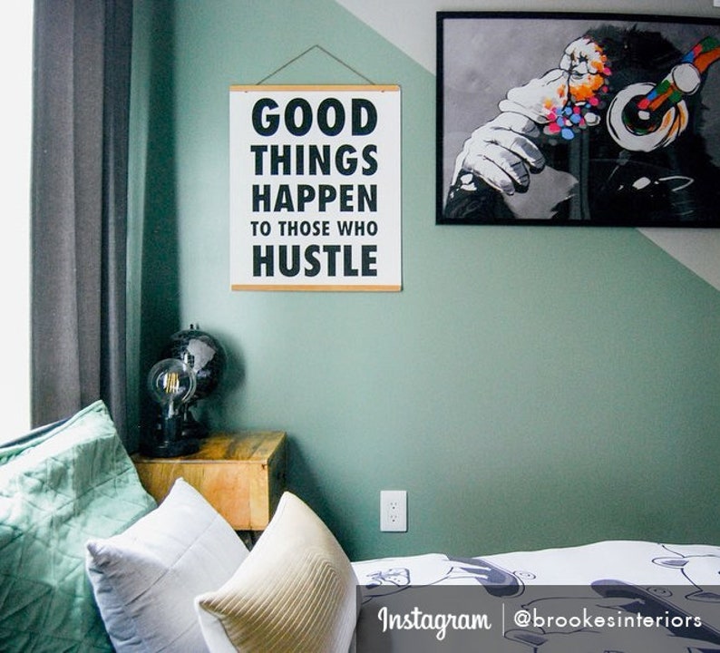 May include: A motivational wall art print with the text "GOOD THINGS HAPPEN TO THOSE WHO HUSTLE" in black on a white background. The print is hanging on a green wall. A framed black and white monkey art print is also visible.