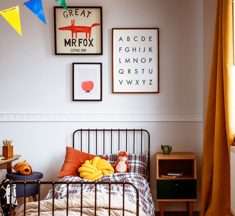 May include: A black metal bed frame with a white and red plaid duvet cover. A yellow knotted pillow and a red fox plush toy are on the bed. There are three framed prints on the wall behind the bed: one with the text "Great Mr. Fox Coming Soon", one with a red apple, and one with the alphabet.