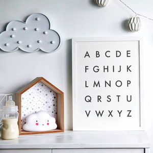 May include: White wooden shelf with a white cloud nightlight and a white frame with the alphabet printed in black. The shelf has a gray and white star pattern background.