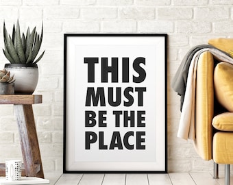 Op de afbeelding: Zwart-wit typografieprint met de tekst "This Must Be The Place" in een zwart frame.
