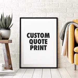 Puede incluir: Un cuadro enmarcado con el texto "CUSTOM QUOTE PRINT" en letras negras en negrita. El cuadro se muestra contra una pared de ladrillos blancos. Un taburete de madera con plantas en macetas y una taza est&aacute;n en primer plano. Un sof&aacute; amarillo es parcialmente visible.