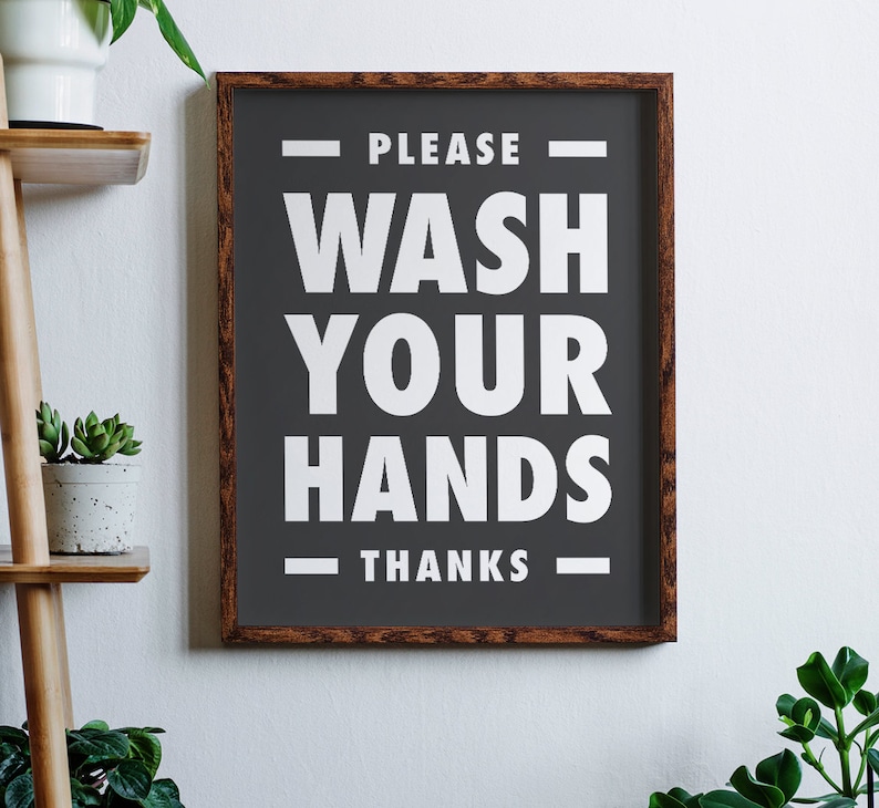 Puede incluir: Un letrero enmarcado con un fondo gris oscuro y texto blanco que dice "PLEASE WASH YOUR HANDS THANKS". El marco es de madera con un acabado marr&oacute;n oscuro. El letrero est&aacute; colgado en una pared blanca.