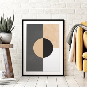 May include: A framed abstract geometric print with a black circle partially overlapping a beige circle, set against a background of gray, beige, and white squares. The print is displayed on a white wall above a wooden table with potted plants.