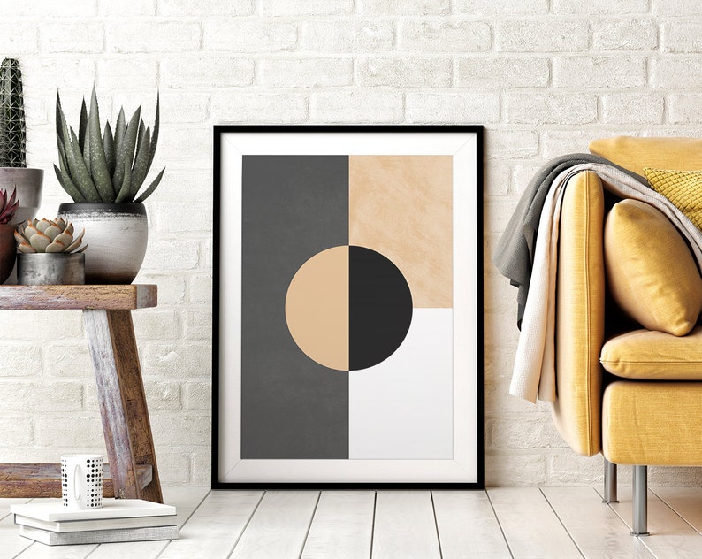 May include: A framed abstract geometric print with a black circle partially overlapping a beige circle, set against a background of gray, beige, and white squares. The print is displayed on a white wall above a wooden table with potted plants.