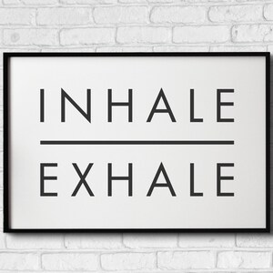 Op de afbeelding: Zwart-wit ingelijste print met de tekst "INHALE EXHALE" in een minimalistische stijl.