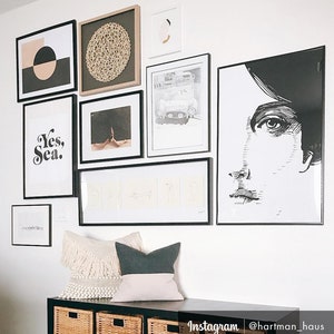 May include: A gallery wall with black frames featuring various prints, including a black and white portrait, a geometric design, a car, and a text print that says "Yes, Sea."