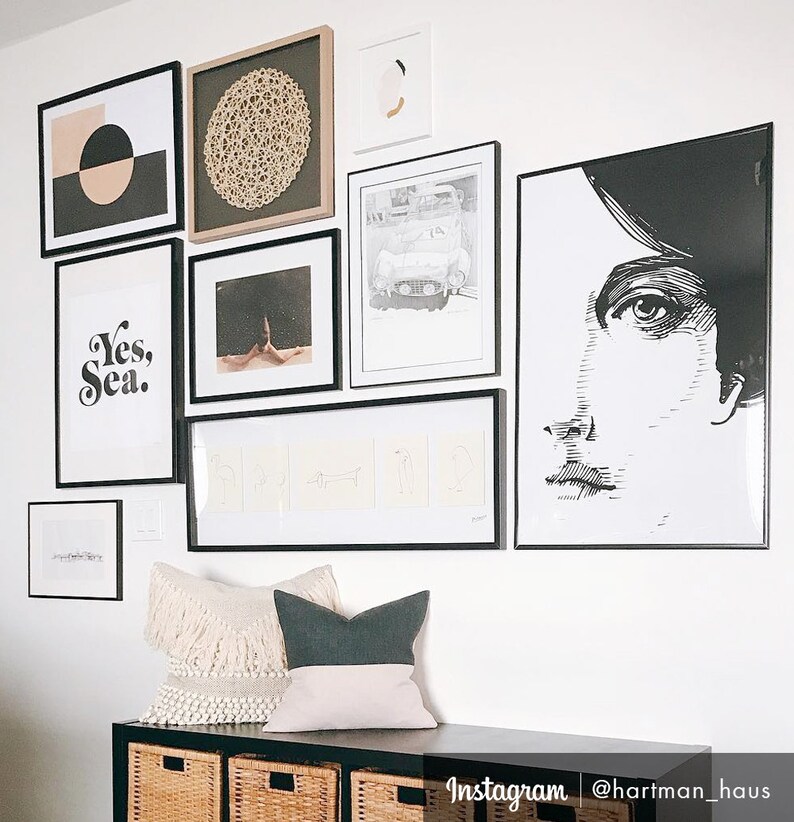 May include: A gallery wall with black frames featuring various prints, including a black and white portrait, a geometric design, a car, and a text print that says "Yes, Sea."