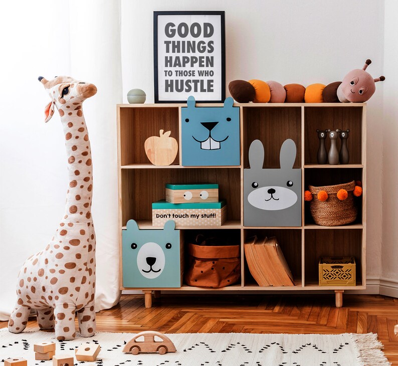 May include: A wooden bookcase with various storage boxes and decorative items. The boxes feature animal faces. A stuffed giraffe and a sign that reads "GOOD THINGS HAPPEN TO THOSE WHO HUSTLE" are also present. A wooden car and blocks are on the floor.