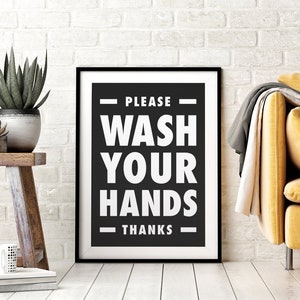 Puede incluir: Un letrero enmarcado en blanco y negro que dice "PLEASE WASH YOUR HANDS THANKS". El letrero est&aacute; en un marco negro y est&aacute; apoyado contra una pared de ladrillos blancos. Un peque&ntilde;o taburete de madera con plantas y una taza est&aacute; en primer plano.