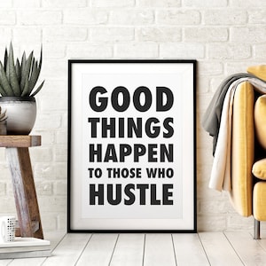 May include: A framed print with the text "GOOD THINGS HAPPEN TO THOSE WHO HUSTLE" in bold black letters. The print is in a black frame and is leaning against a white brick wall. A yellow sofa and plants are in the background.