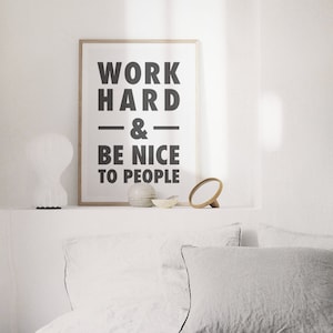 Puede incluir: Una impresi&oacute;n enmarcada con el texto "WORK HARD & BE NICE TO PEOPLE" en letras negras sobre un fondo blanco. La impresi&oacute;n est&aacute; sentada en un estante blanco con una l&aacute;mpara blanca, un peque&ntilde;o cuenco de cer&aacute;mica y un espejo de madera.