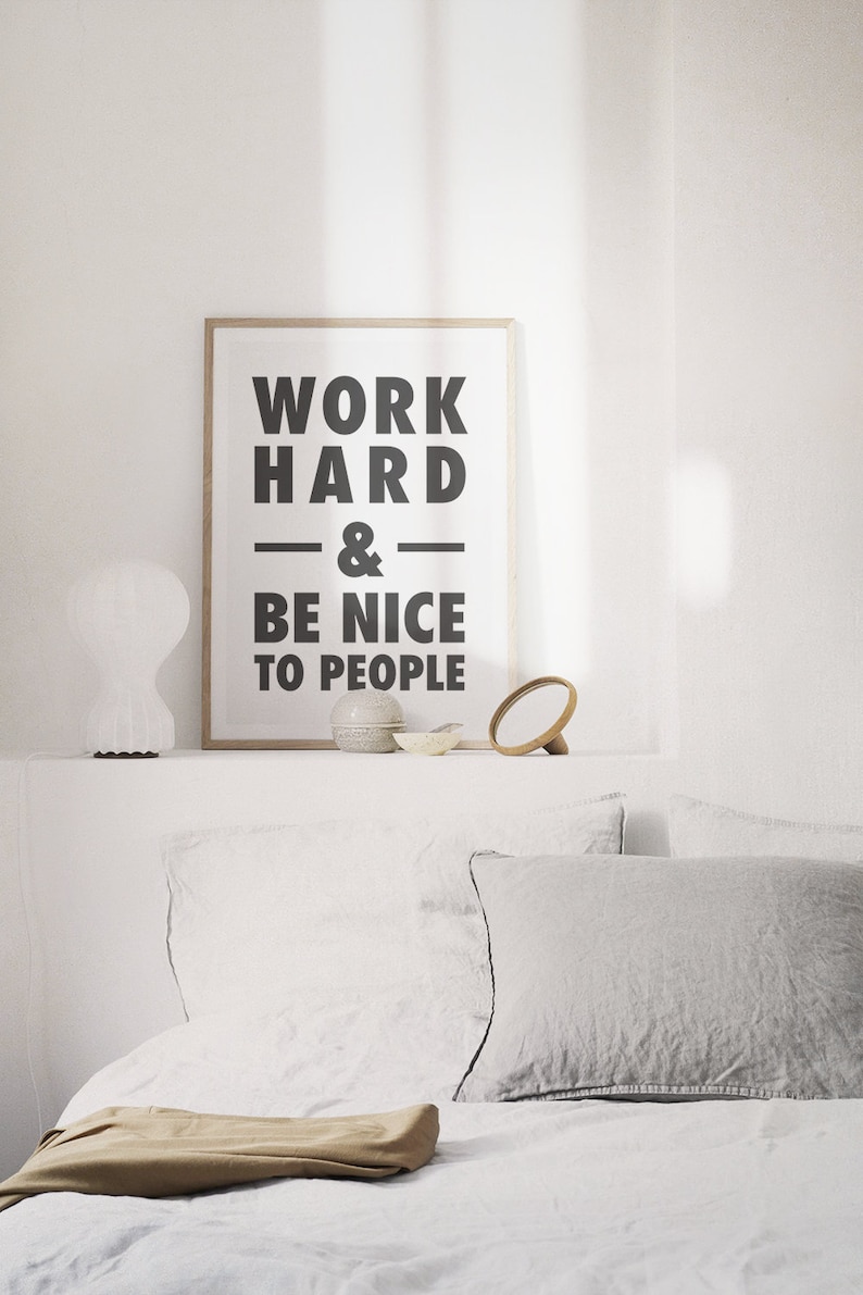 Puede incluir: Una impresi&oacute;n enmarcada con el texto "WORK HARD & BE NICE TO PEOPLE" en letras negras sobre un fondo blanco. La impresi&oacute;n est&aacute; sentada en un estante blanco con una l&aacute;mpara blanca, un peque&ntilde;o cuenco de cer&aacute;mica y un espejo de madera.