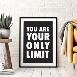 Könnte beinhalten: Ein gerahmter Schwarz-Weiß-Druck mit dem Text "YOU ARE YOUR ONLY LIMIT" in fetten weißen Buchstaben. Der Druck wird an einer weißen Backsteinmauer mit einem Holzschemel mit Pflanzen und einer Tasse im Vordergrund angezeigt.