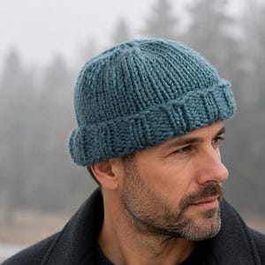 May include: A teal blue knit beanie with a thick, folded ribbed cuff. The hat is constructed from a chunky yarn with a vertical ribbed texture that extends from the crown down to the wide, turned-up brim, providing a textured appearance.