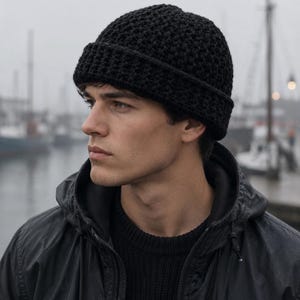 May include: A solid black beanie crafted with a textured, grid-like crochet pattern. The hat features a thick, folded cuff that sits securely around the head, providing a structured look with a consistent dark tone throughout the entire piece.