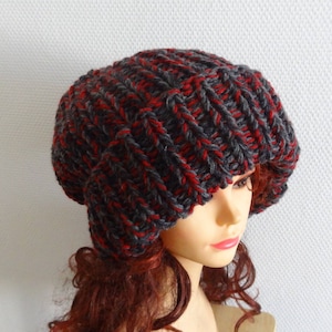 May include: A slouchy beanie hat in a grey and red colour combination. The hat is knitted with a thick yarn and has a loose, slouchy fit.