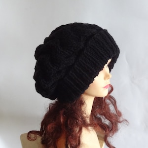 Puede incluir: Un gorro de punto negro con un patrón de trenza. El gorro es holgado y tiene una forma redonda y grande.