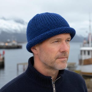 Puede incluir: Un gorro de punto azul profundo con un borde grueso y enrollado. El gorro presenta una textura acanalada vertical en toda la corona y una parte superior lisa y redondeada. El material parece ser un hilo suave y grueso de ajuste firme.