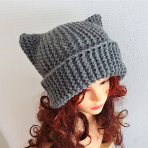 May include: Gray knitted beanie with cat ears. The beanie is made of a soft, textured yarn and has a slouchy fit.
