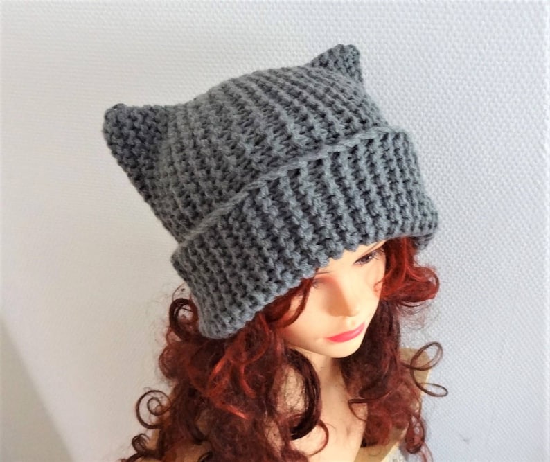 May include: Gray knitted beanie with cat ears. The beanie is made of a soft, textured yarn and has a slouchy fit.